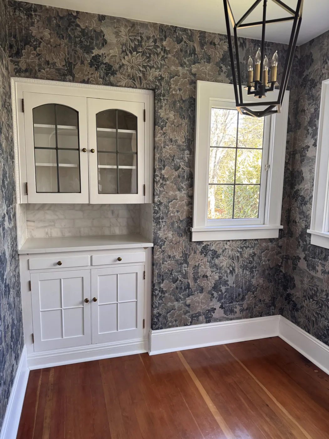 Dining room with vintage forest-print wallpaper around a built-in hutch