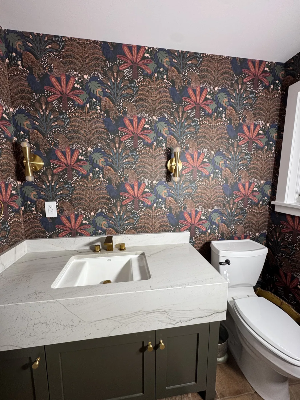 Powder room with bold jungle leopard wallpaper and brass sconces